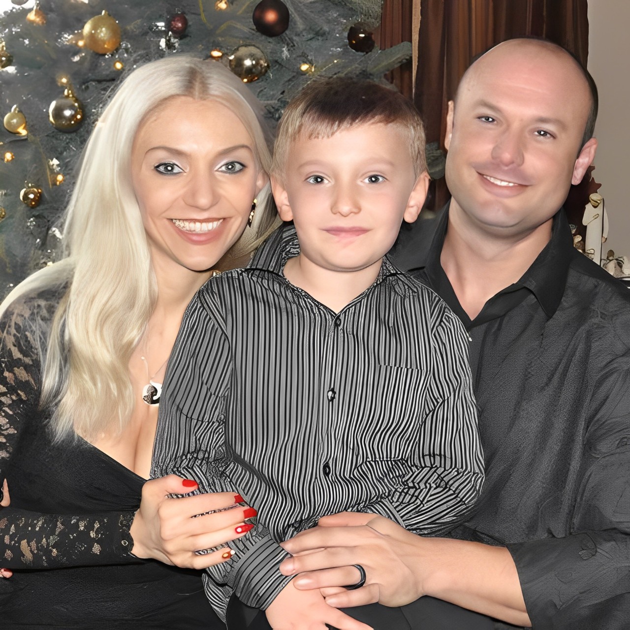 A man and woman holding a boy in front of a christmas tree.
